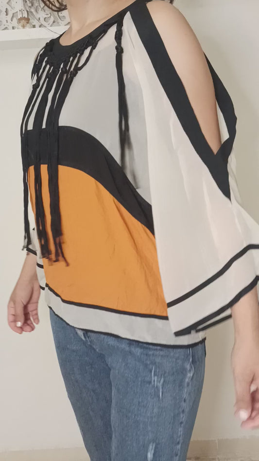 Gros coup de cœur pour cette pièce vintage qui ne passe pas inaperçue ! Ses découpes aux épaules, son mix de couleurs (blanc, noir et orange vif) et surtout ses franges audacieuses en font un top vraiment unique