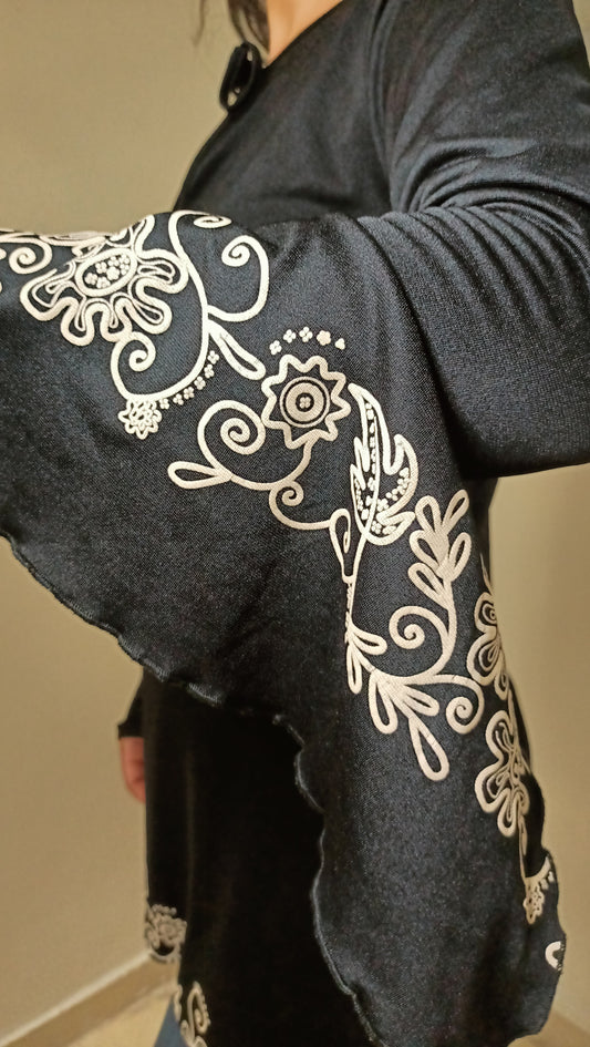 superbe tunique noire, sublimée par de magnifiques broderies florales blanches. Les manches évasées ajoutent une touche de poésie et un charme vintage indéniable.